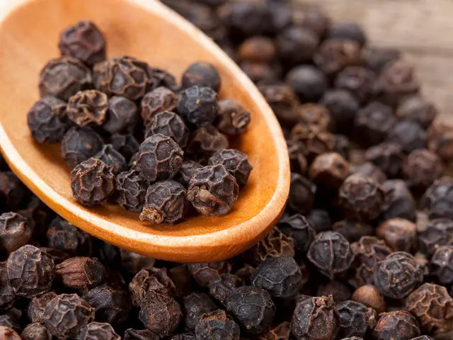 Whole black peppercorns in a wooden spoon, the source of piperine